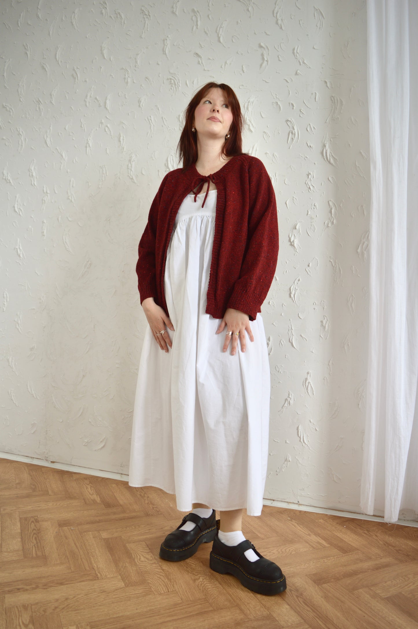 Full length view of model wearing The Cosy Cardi in red, styled with white dress and black shoes