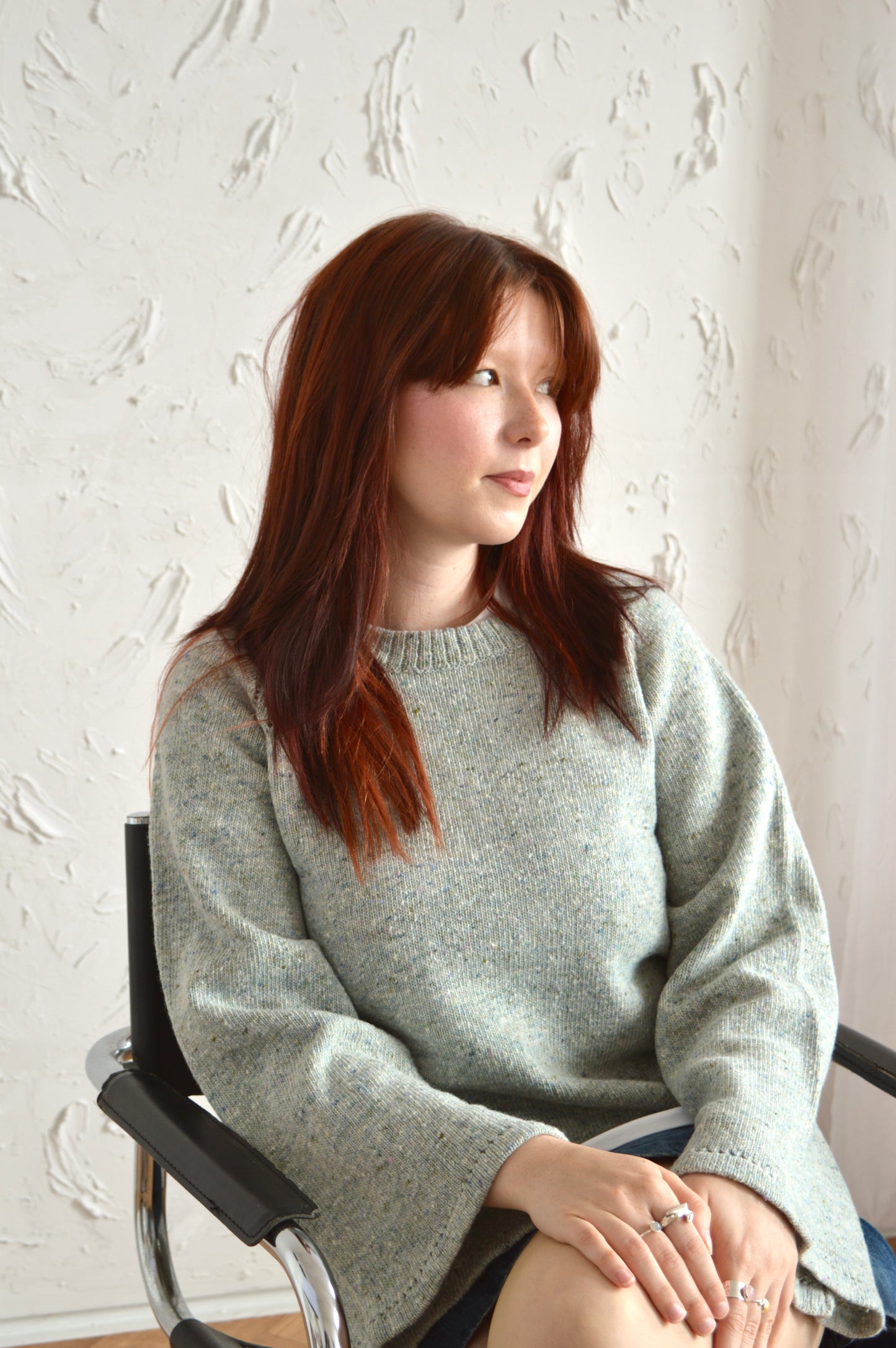 Model wearing The Bell Sweater in light grey sat down on a chair