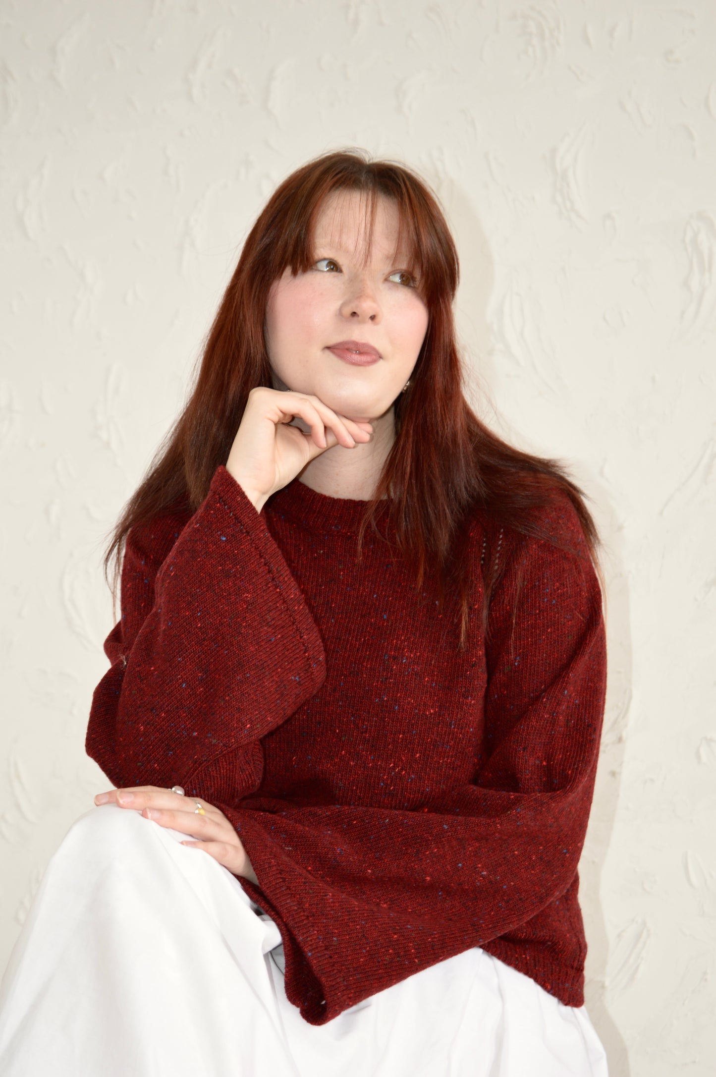 Model sits down wearing The Bell Sweater in red