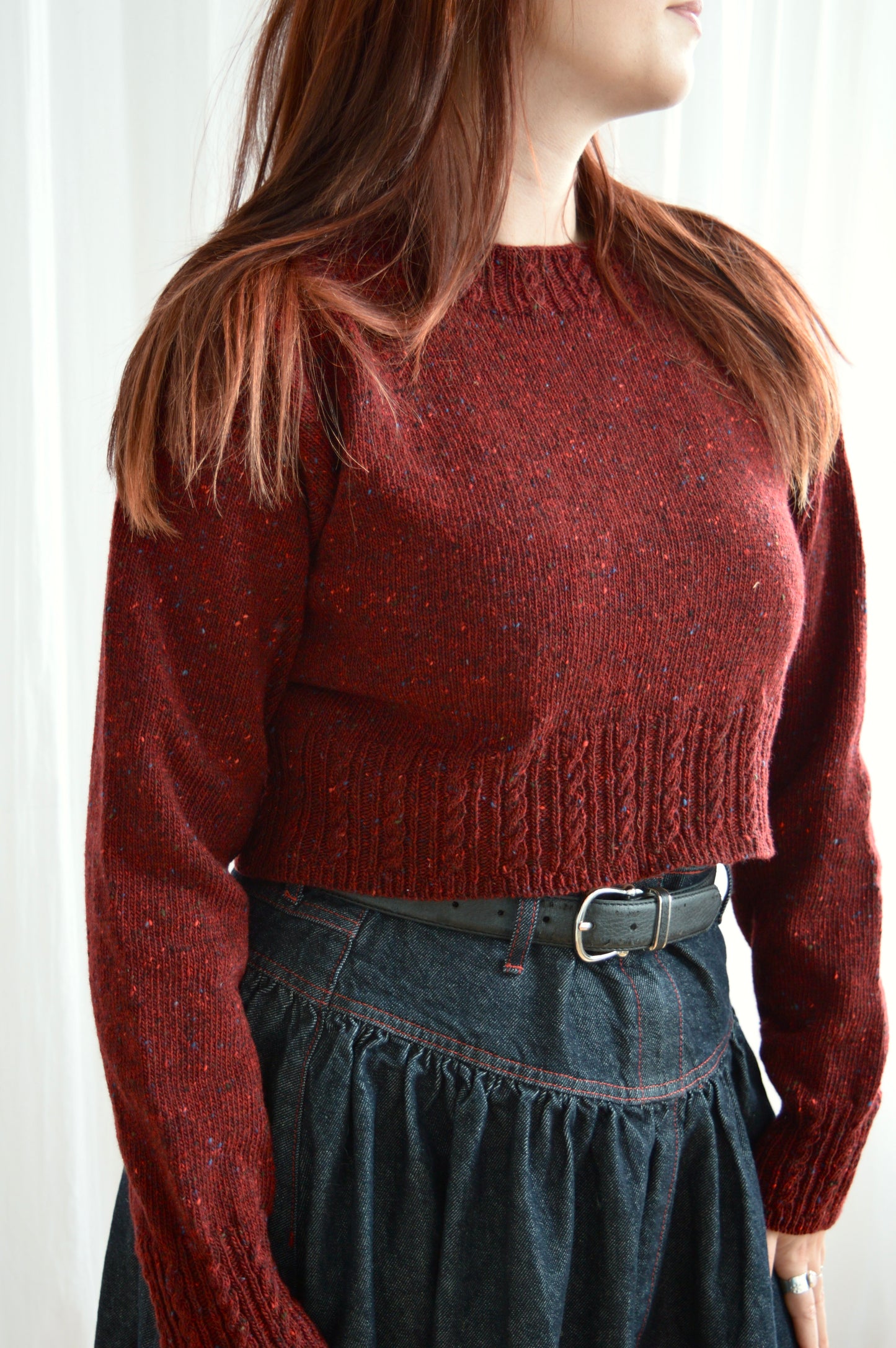 Close up side angle of model wearing The Cable Sweater in red