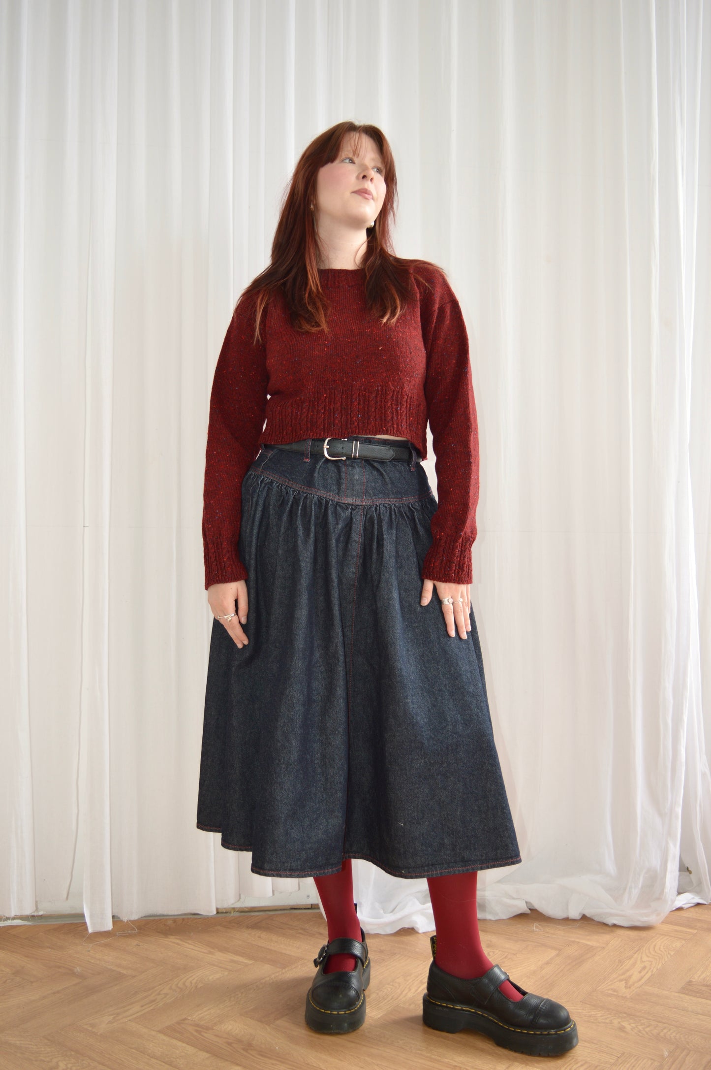 Full length view of model wearing The Cable Sweater in red, styled with denim skirt, red tights and black shoes
