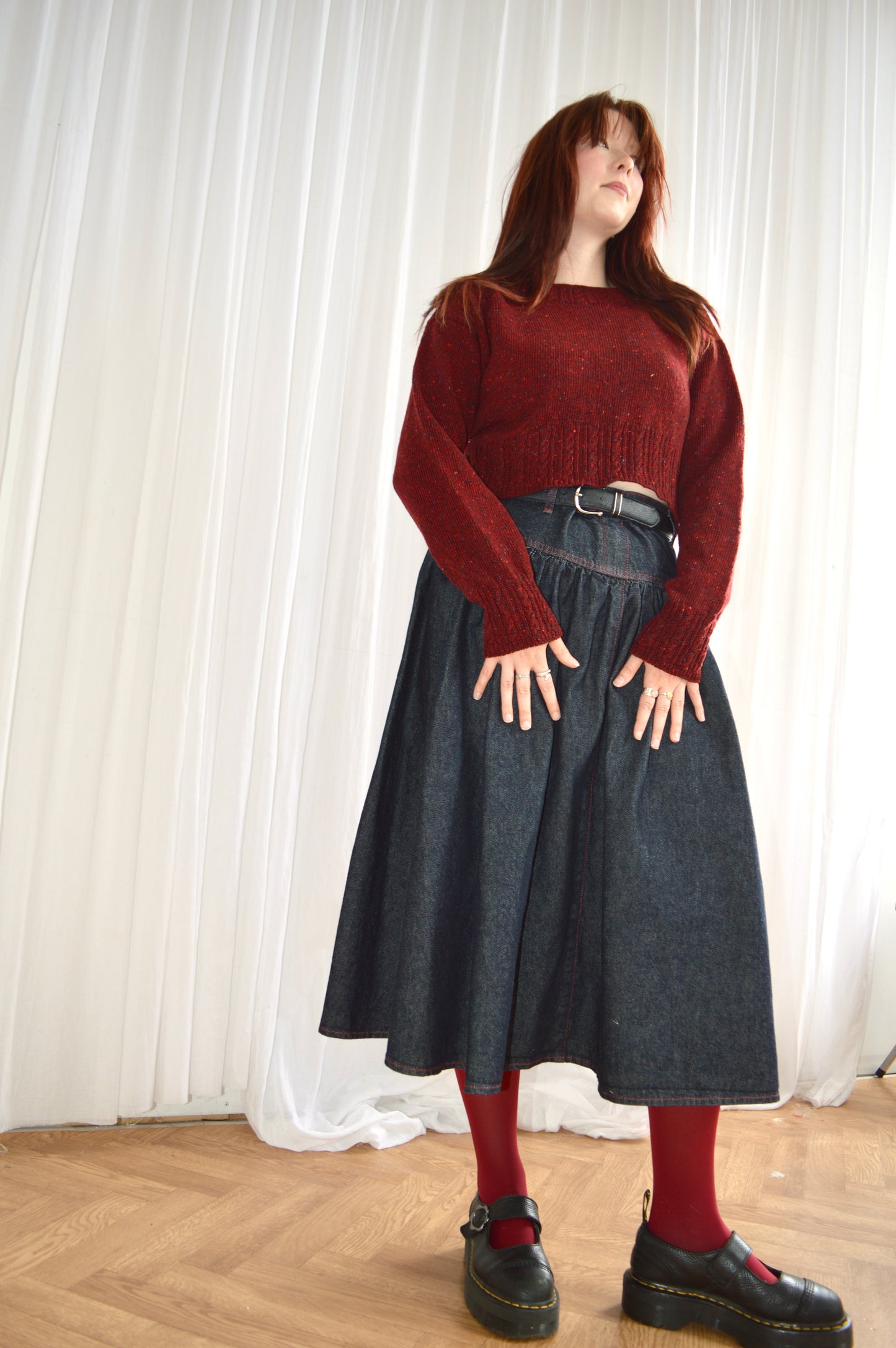 Low angle of model wearing red Cable sweater, styled with denim skirt, red tights and black shoes