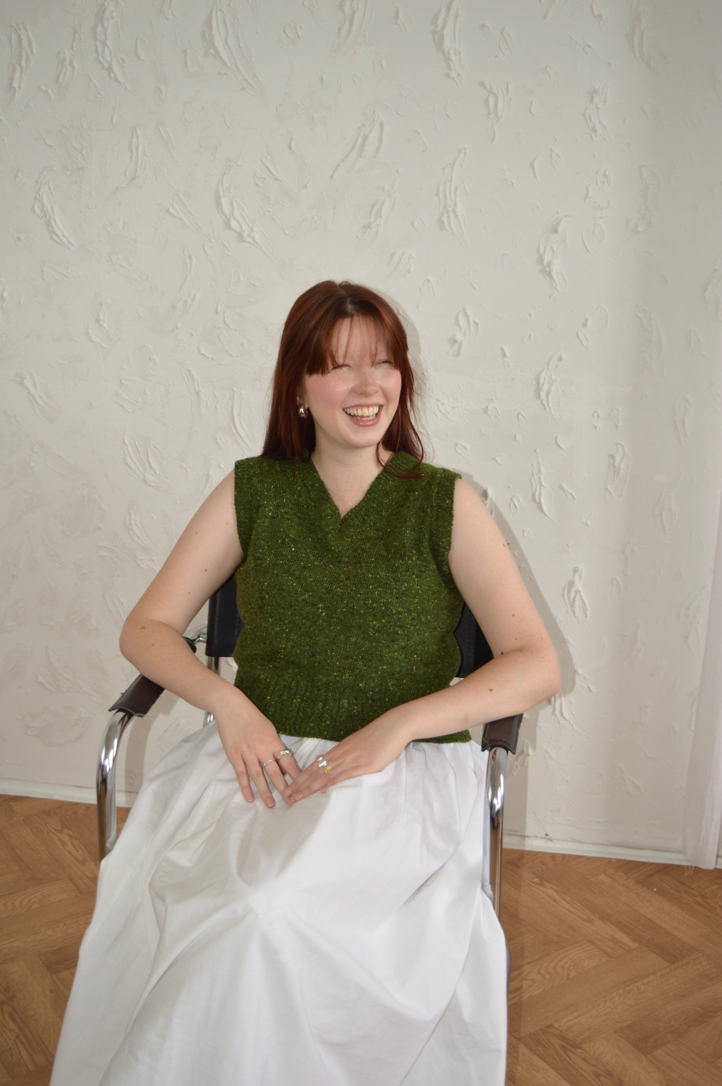 Model seated wearing green Cable Vest, photographed from a high angle.