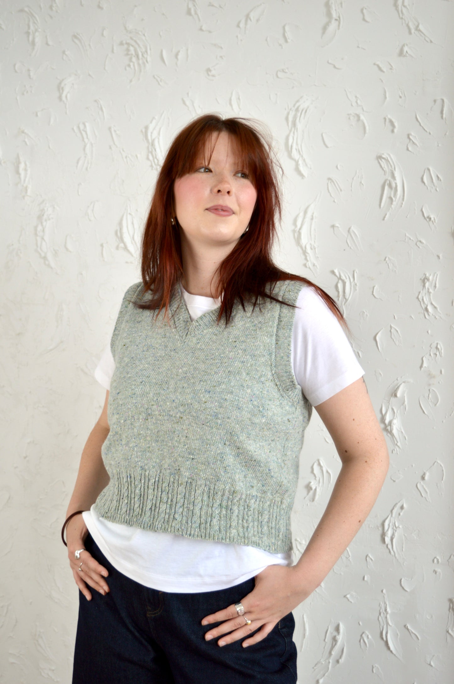 Model wears The Cable Vest in light grey, posing with hands in pockets