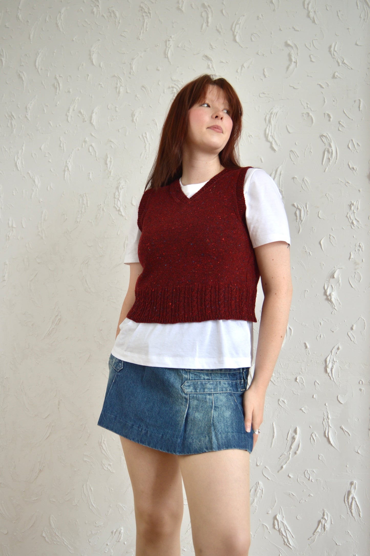 Model wearing The Cable Vest in red, styled with a white T-shirt and denim skirt.