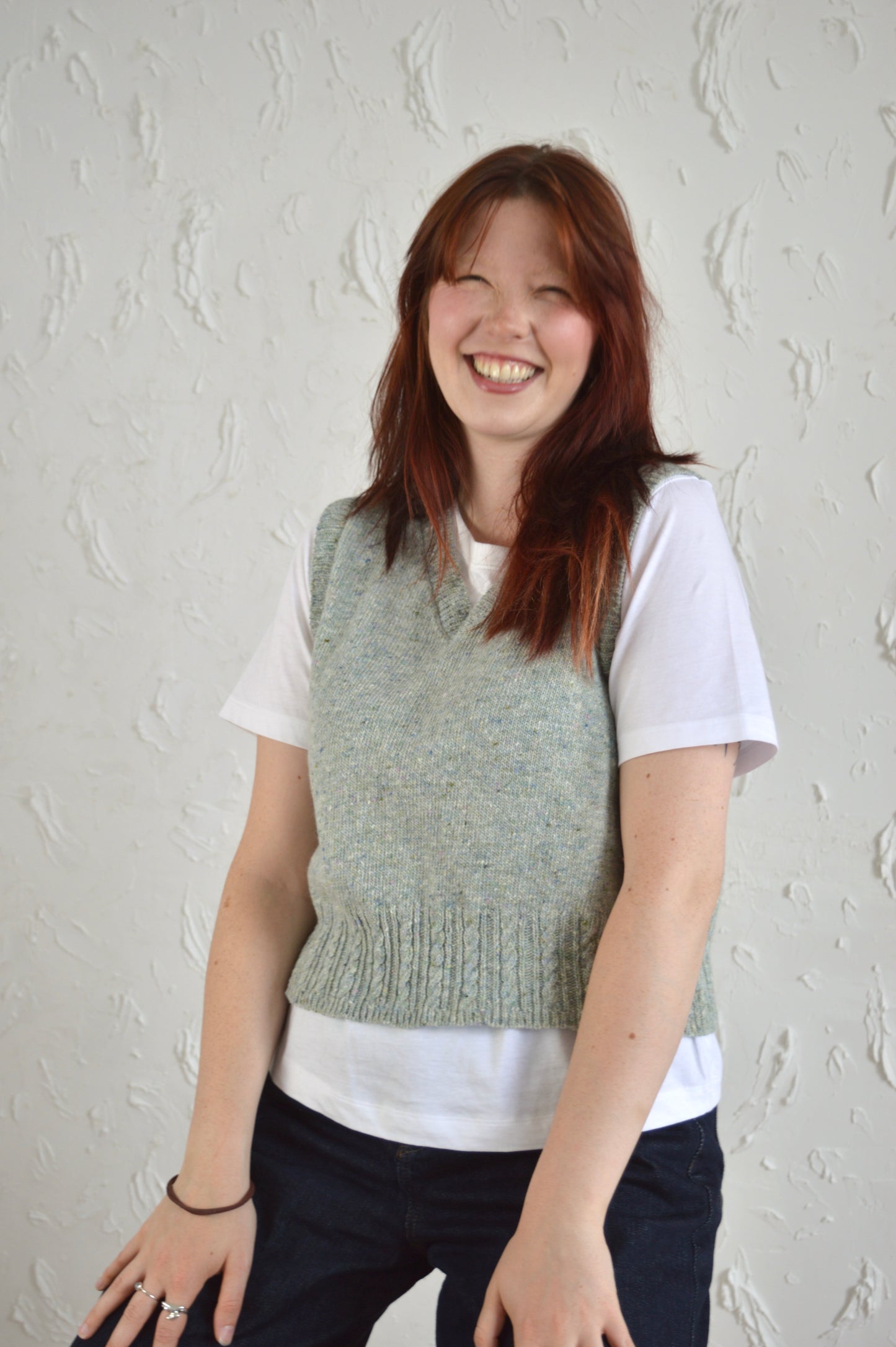 Model wearing The Cable Vest, smiling while sitting on a stool