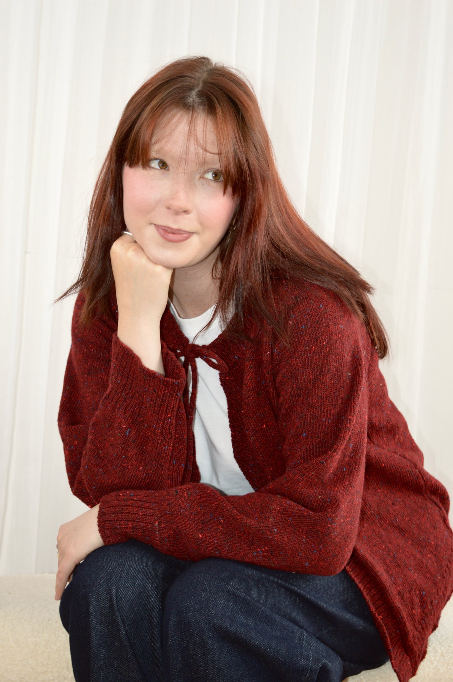 Model sitting wearing The Cosy Cardi in red