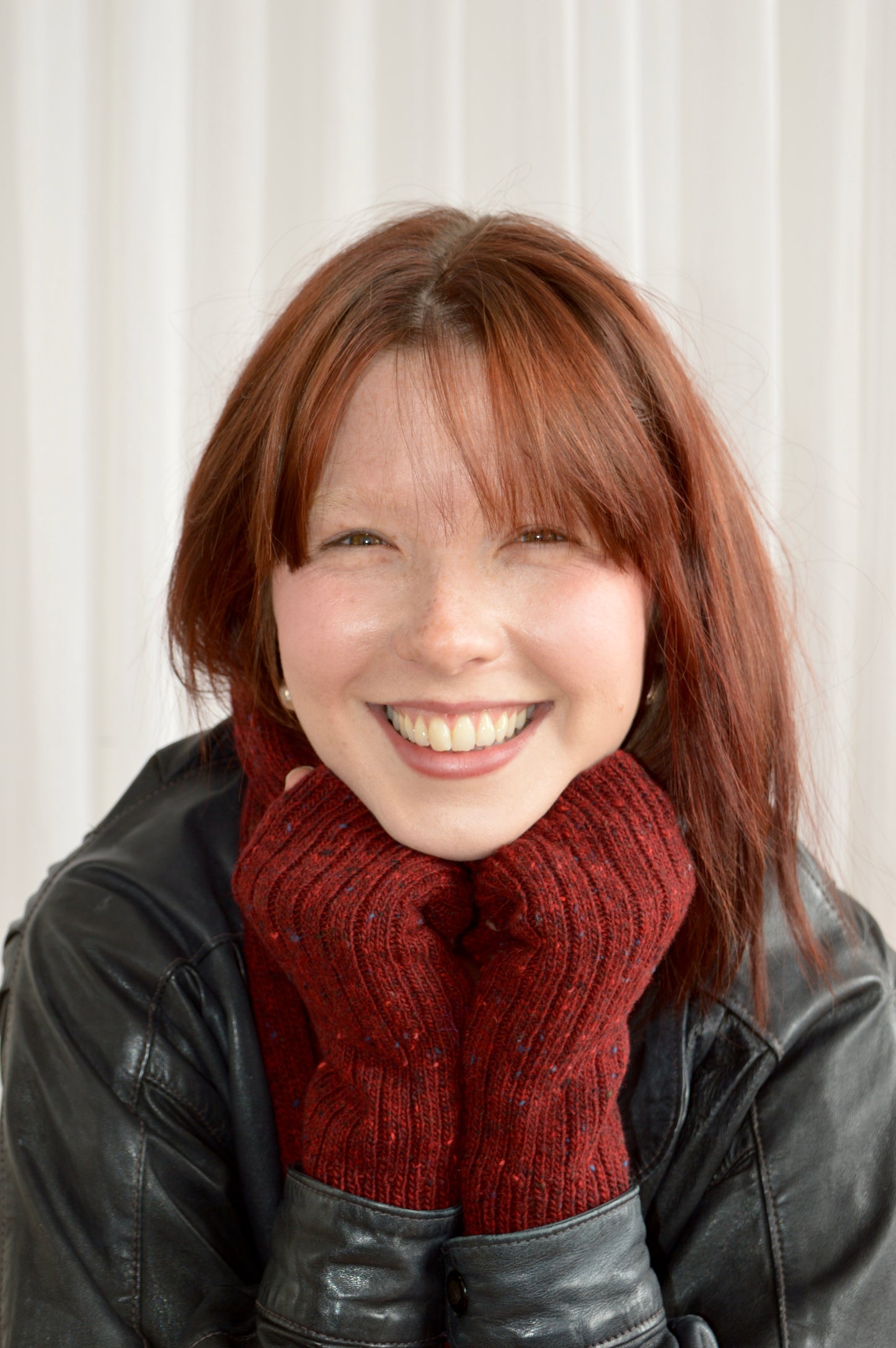 Model smiling with both hands under chin wearing The Fingerless Gloves in red