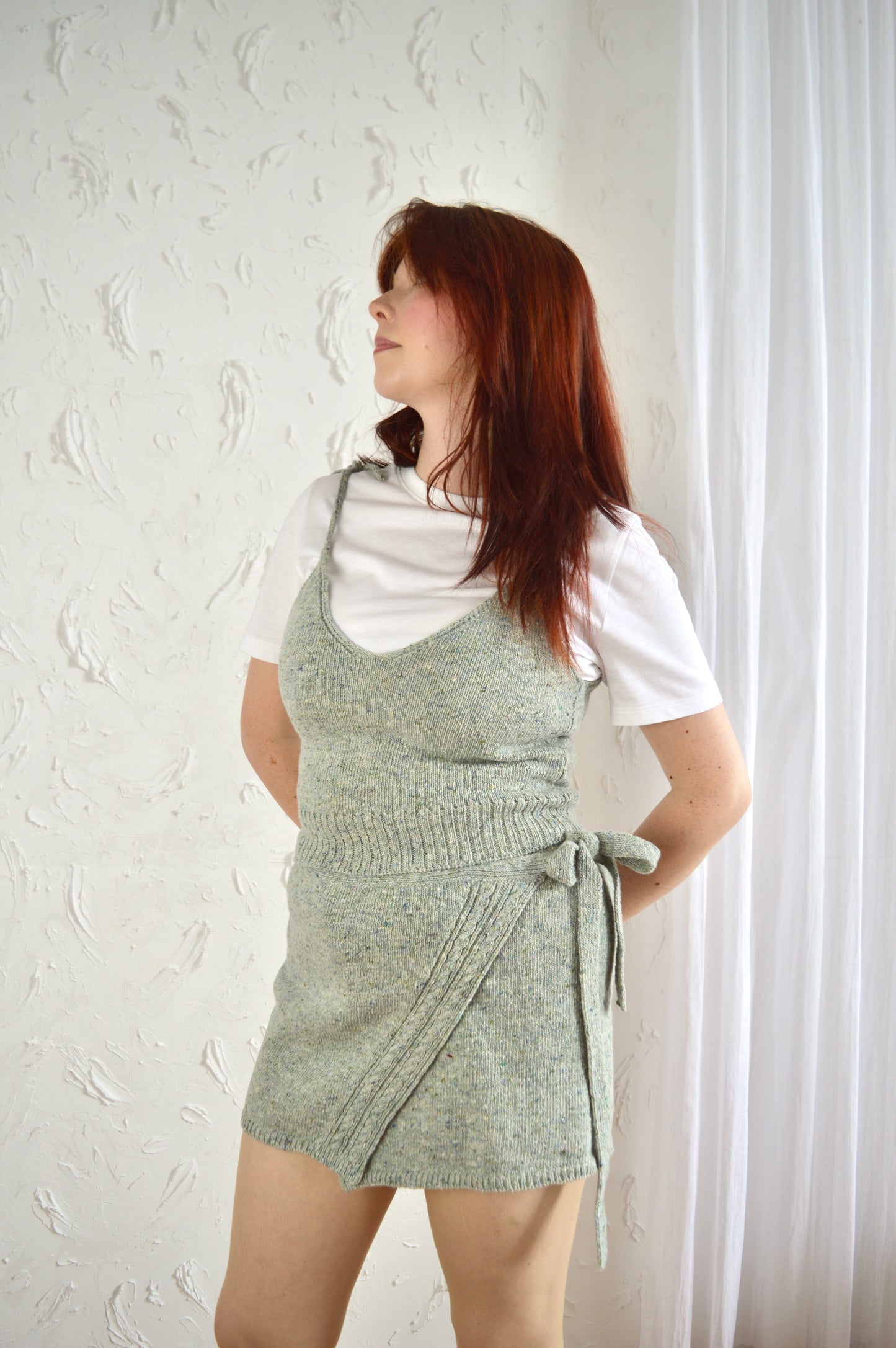Model wearing The Wrap Skirt in light grey styled with The Tie Cami and white T-shirt, hands positioned behind back.