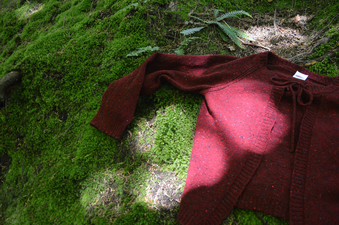 Red Cosy cardi laid out on moss with the sun shining down