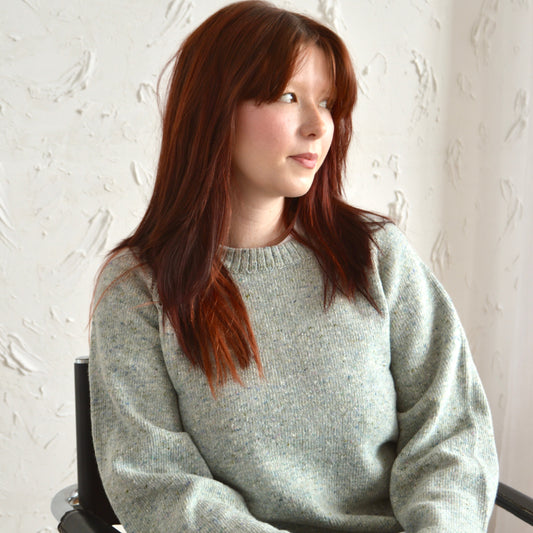 Woman wearing the bell sweater in grey, sat down