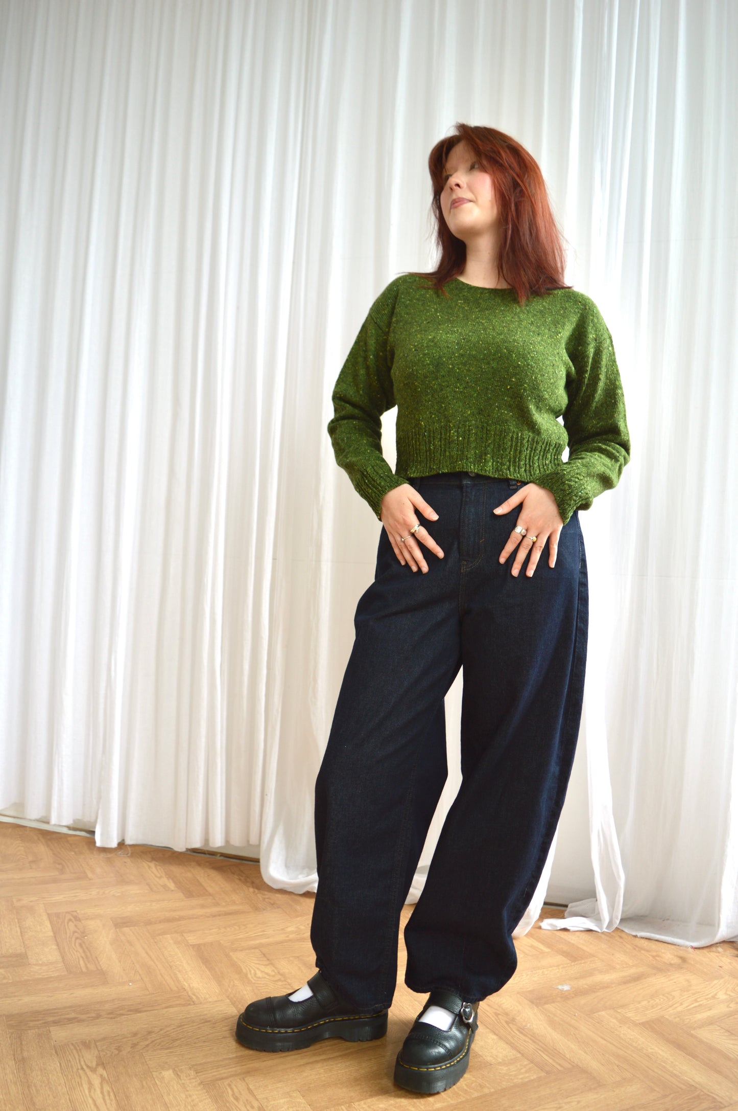 Full length view of model wearing The Cable Sweater in green, styled with dark denim jeans and black shoes