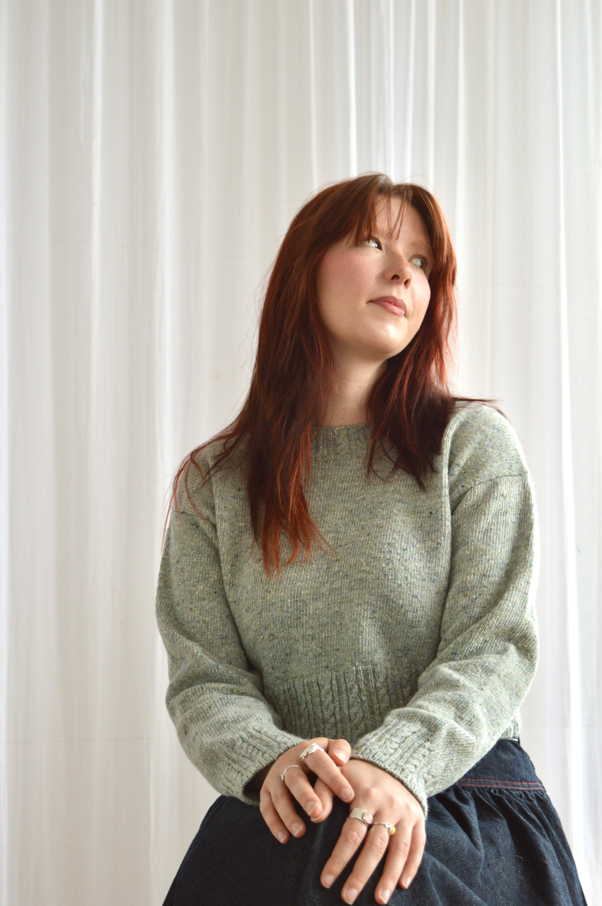 Model wearing The Cable Sweater in light grey sat down with hands on lap