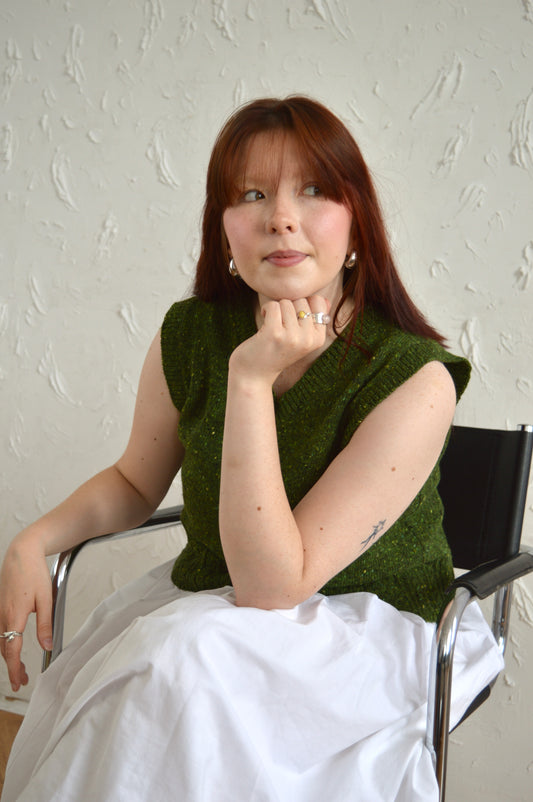 Model seated wearing The Cable Vest in green