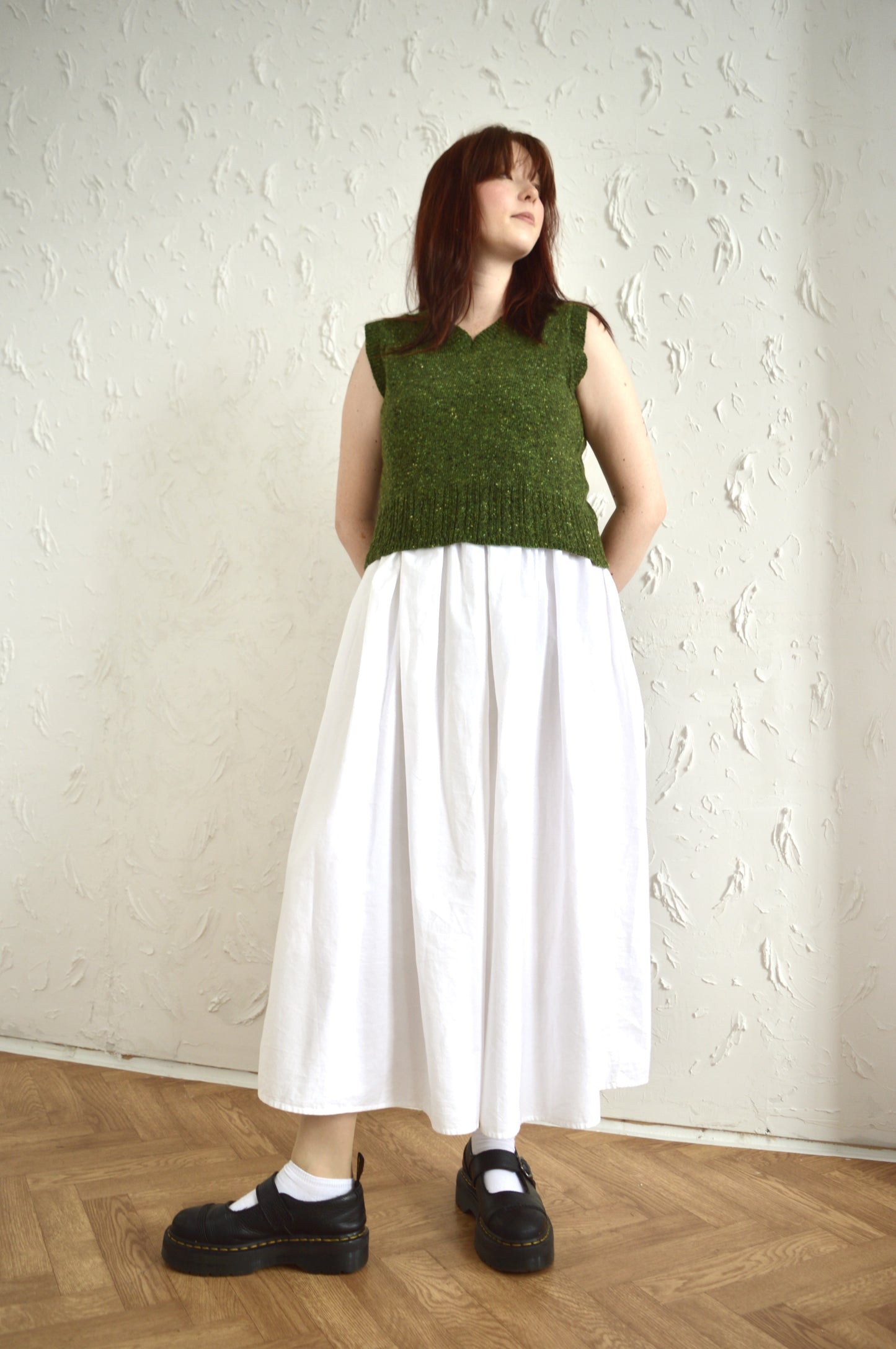 Full-body shot of model styled in green Cable Vest, white skirt, and black shoes.