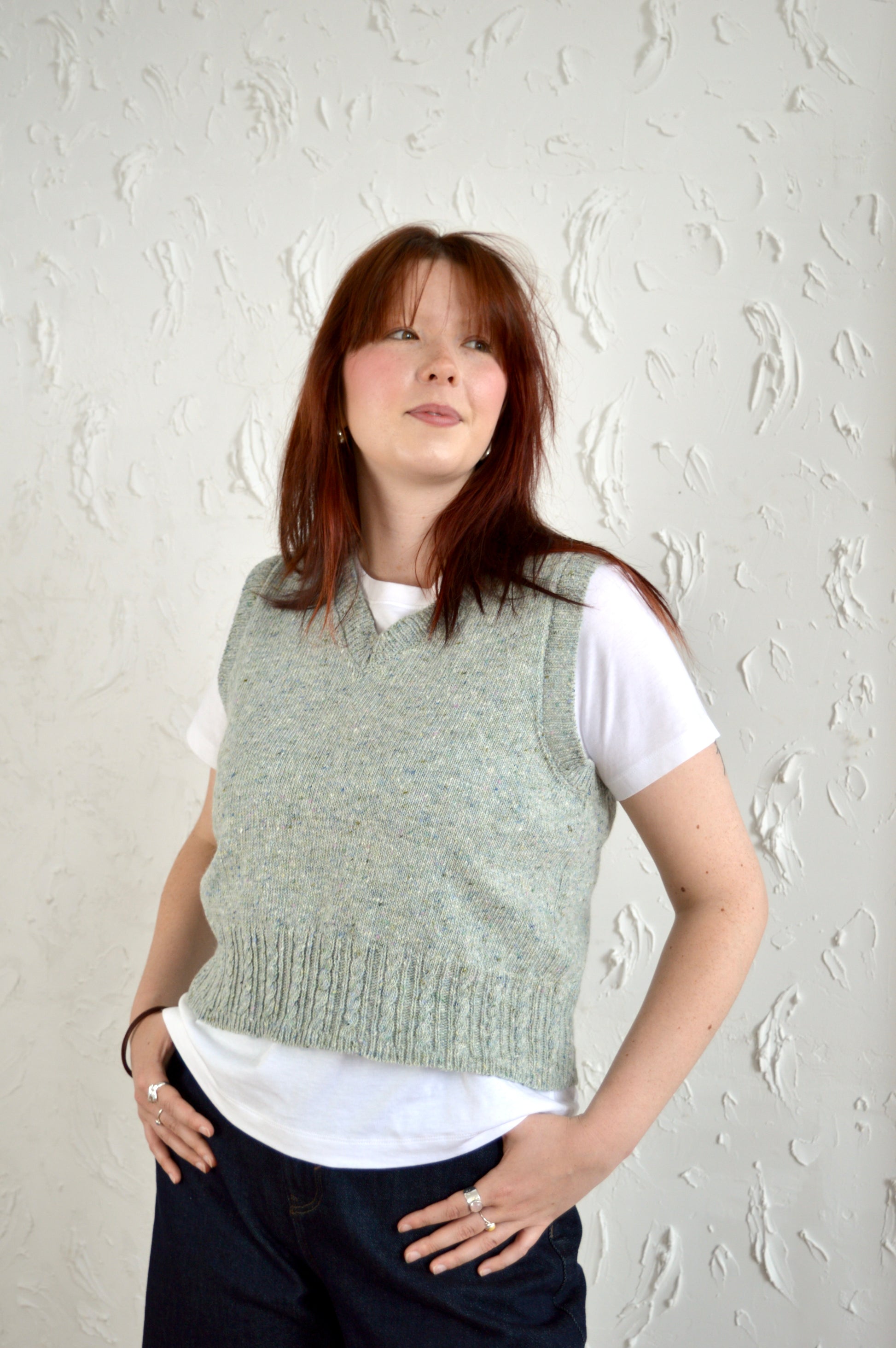 Model wears The Cable Vest in light grey, posing with hands in pockets