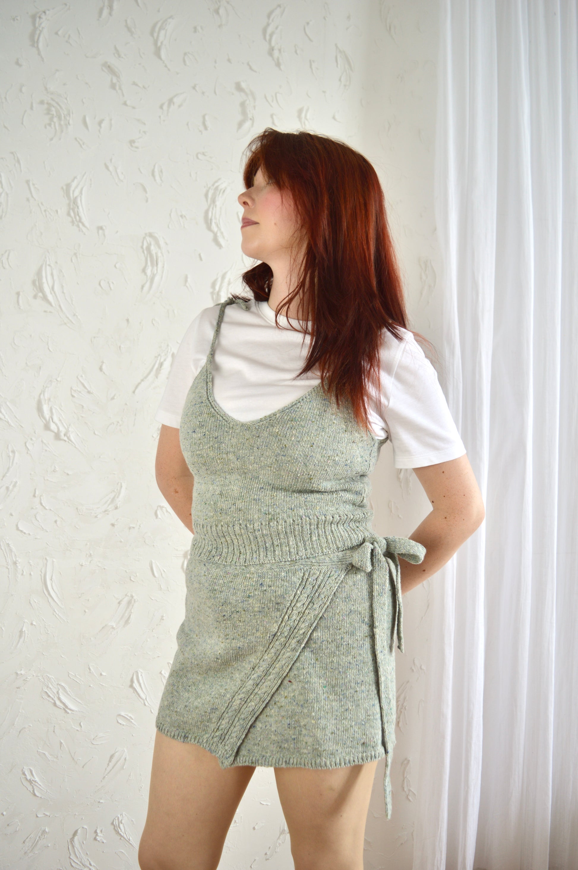 Model wearing The Wrap Skirt in light grey styled with The Tie Cami and white T-shirt, hands positioned behind back.